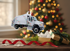 A white garbage truck Christmas ornament decorated with colorful holiday string lights, hanging by a red ribbon on a white background.