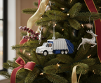 White and blue garbage truck ornament hanging on a decorated Christmas tree.